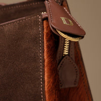 Close-up of a brown leather Danilos bag with hair on leather with gold zipper and logo detail.