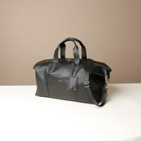 Black leather travel bag on a white surface with a beige background
