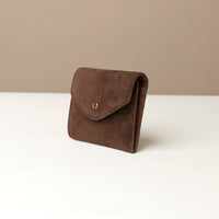 Brown suede wallet on a white surface with a beige background