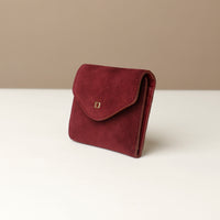 Red suede wallet with a gold emblem on a white surface with a beige background