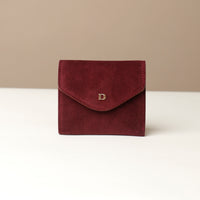 Red suede wallet with a gold logo on a white surface and beige background