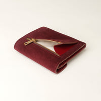 Maroon wallet with gold zipper on a light beige background