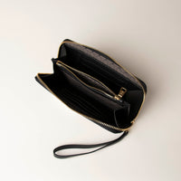 upper view of a open black Danilos wallet Carlota with a visible handle drop and gold zippers in a beige background