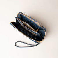 upper view of a open blue Danilos wallet Carlota with a visible handle drop and gold zipper in a beige background