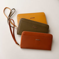 front view of a green, brown and yellow Danilos wallet Carlota with a visible handle drop in a beige background