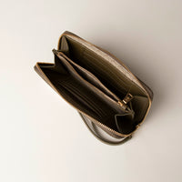 upper view of a open green Danilos wallet Carlota with a visible handle drop and a gold zipper in a beige background