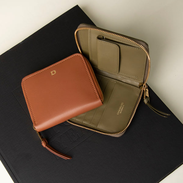 A brown and green zurich sr wallet with a zippered seal, placed on a dark book with a visible danilos leather logo.